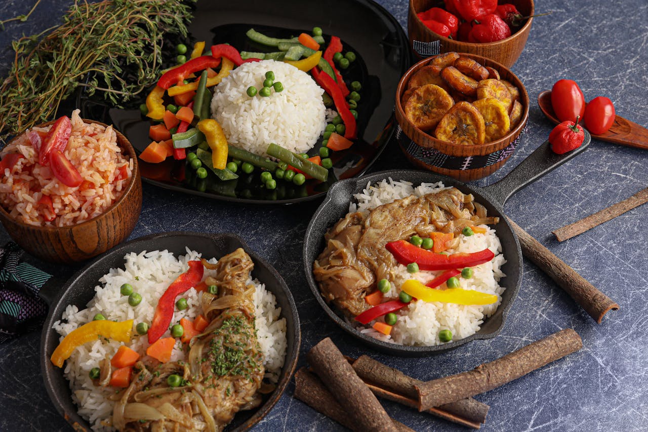 about-us A vibrant display of traditional rice dishes with vegetables, plantains, and chicken in iron pans.