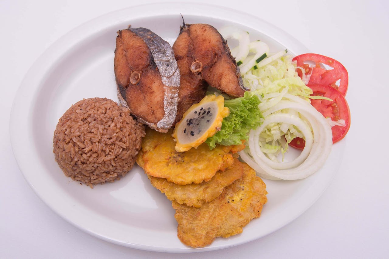 Delicious fried fish with rice, plantains, and fresh salad on a white plate.